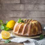 Ciambella al limone soffice: la ricetta facile senza burro 1 In primo piano su uno sfondo rustico di un tavolo da cucina c'รจ una ciambella al limone decorata con dello zucchero a velo.