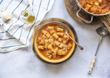 su piano da cucina pasta e patate, pentola con pasta e patate, un piatto pronto con cucchiaio, 1 mestolo, 1 canovaccio, aglio e 1 piccolo dosatore di olio EVO