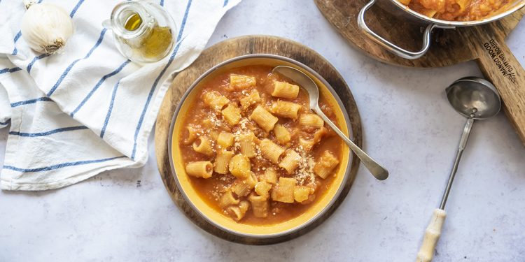 su piano da cucina pasta e patate, pentola con pasta e patate, un piatto pronto con cucchiaio, 1 mestolo, 1 canovaccio, aglio e 1 piccolo dosatore di olio EVO