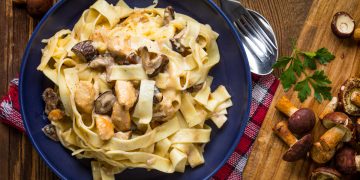 piatto blu con tagliatelle ai funghi e vassoio con porcini