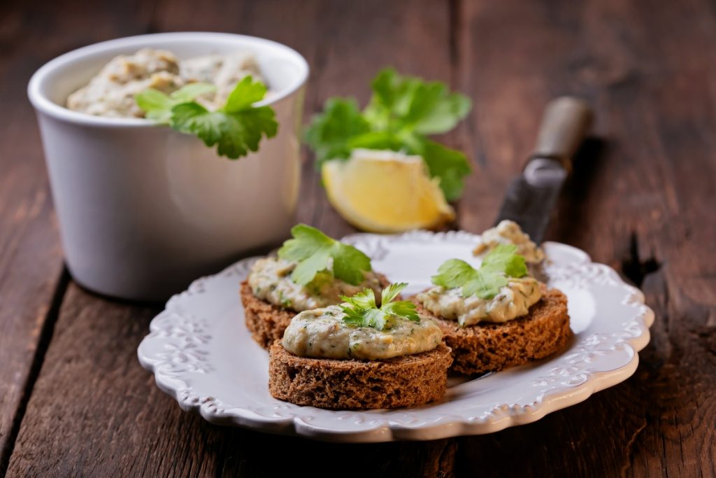 cosa mangio stasera: piatto bianco su un tavolo con 3 bruschette di mousse di tonno, 1 limone e una ciotola di tonno in scatola