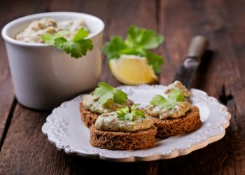 piatto bianco su un tavolo con 3 bruschette di mousse di tonno, 1 limone e una ciotola di tonno in scatola