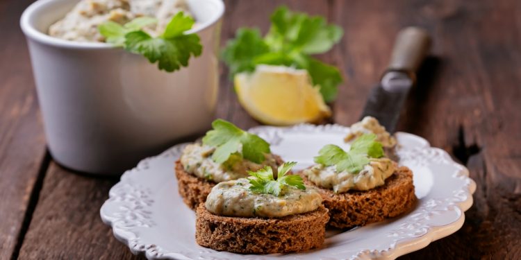 piatto bianco su un tavolo con 3 bruschette di mousse di tonno, 1 limone e una ciotola di tonno in scatola