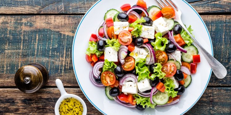 su tavolo di legno un piatto bianco con un'insalata greca e vicino una pepiera