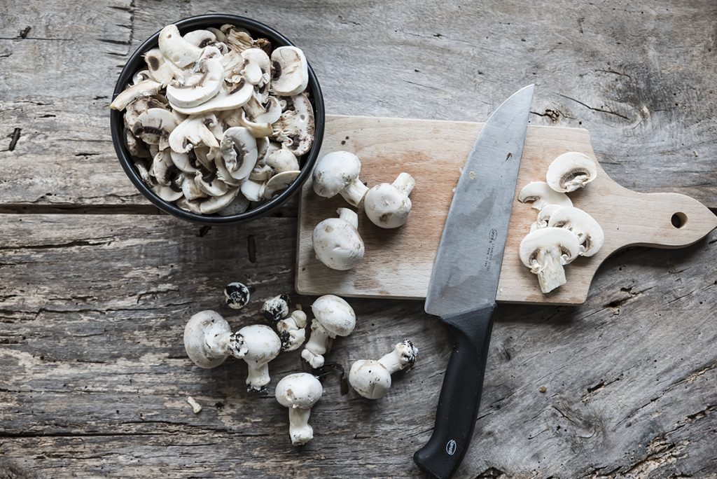 in primo piano su un tagliere di legno dei funghi champignon e un coltello