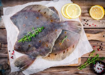 su base di legno tagliere di legno con carta forno e sopra due rombi al forno con fette di limone
