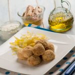 su un piatto rettangolare chiaro una porzione di polpette di tonno e ricotta e patate sottili, una bolligli di olio