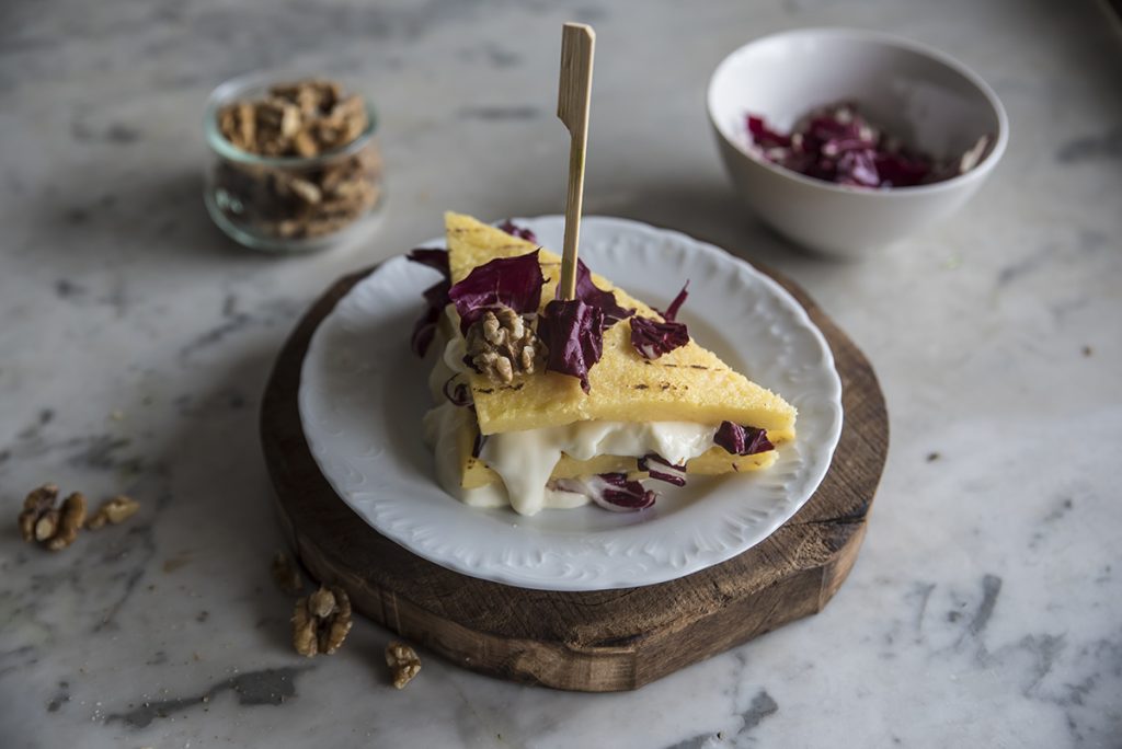 su base di legno tonda piatto bianco con crostino di polenta e uno spiedino