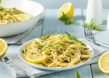 un piatto bianco con linguine al limone, prezzemolo e fetta di limone