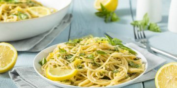un piatto bianco con linguine al limone, prezzemolo e fetta di limone