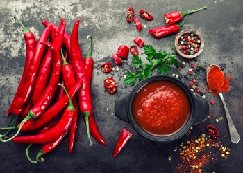 Peperoncini interi, ciotola con salsa rossa al peperoncino, ciotola con grani e cucchiaino di peperoncino in polvere