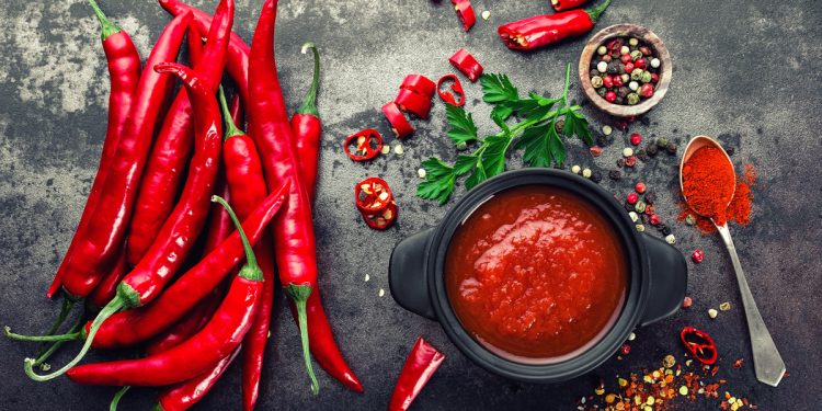 Peperoncini interi, ciotola con salsa rossa al peperoncino, ciotola con grani e cucchiaino di peperoncino in polvere