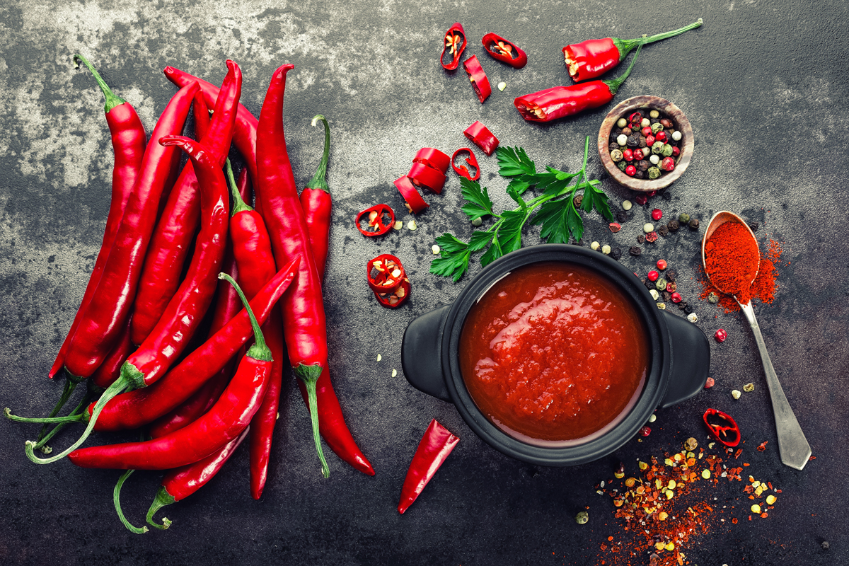 Peperoncini interi, ciotola con salsa rossa al peperoncino, ciotola con grani e cucchiaino di peperoncino in polvere