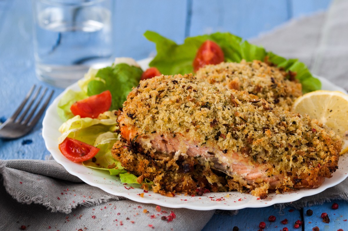 piatto con salmone in crosta, foglie di lattuga, pomodorini e mezzo limone