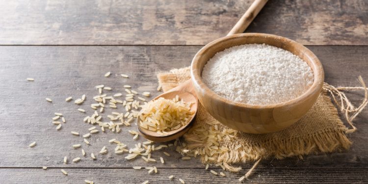 su piano di legno una ciotola di legno con del riso bianco, chicchi di riso sparsi intorno