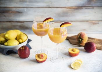 due calici con Virgin Bellini e uno spicchio di pesca, pesche e limoni sparsi