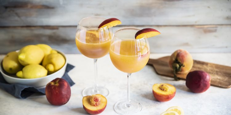 due calici con Virgin Bellini e uno spicchio di pesca, pesche e limoni sparsi
