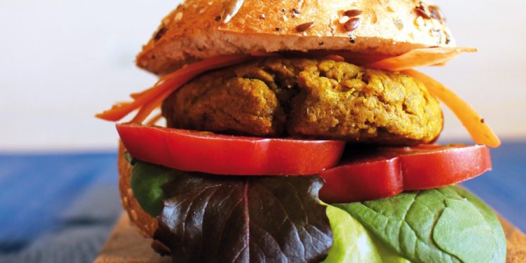 su base di legno un paffuto hamburger di ceci e lenticchie, con pomodoro e foglie di insalata