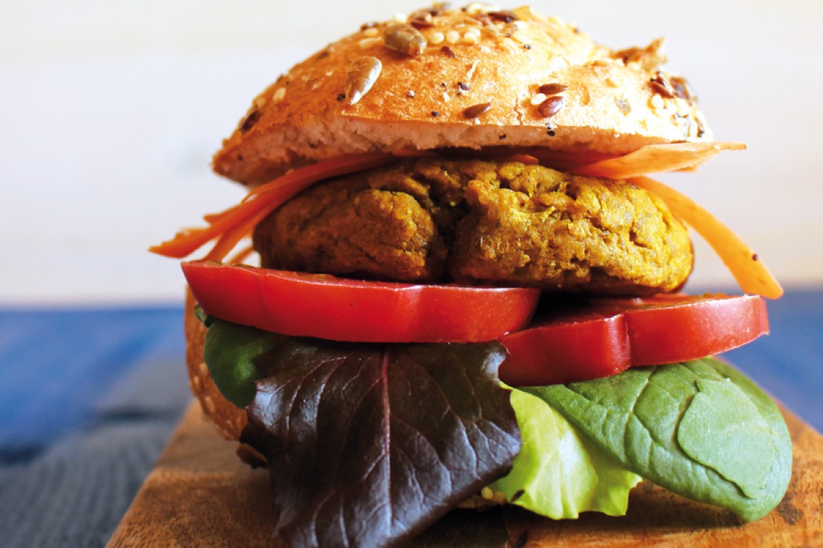 su base di legno un paffuto hamburger di ceci e lenticchie, con pomodoro e foglie di insalata