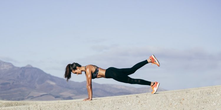 donna al mare con un leggings nero che esegue un plank alzato per dimagrire le gambe