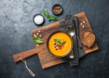tagliere di legno con ciotola piena di crema di zucca e crostini accanto