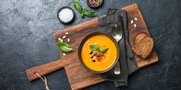 tagliere di legno con ciotola piena di crema di zucca e crostini accanto