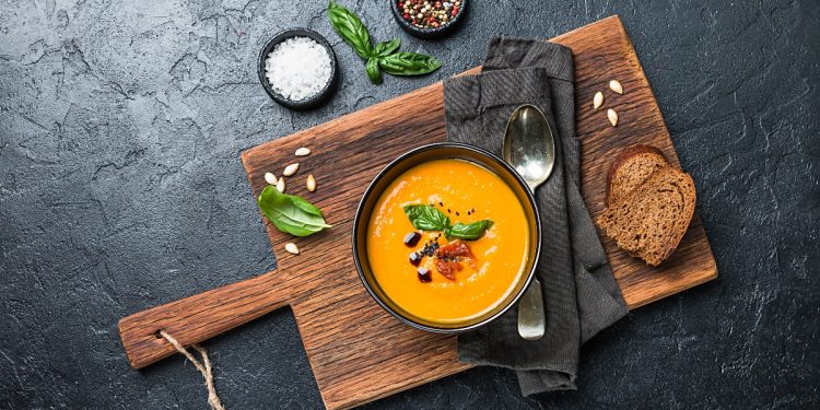 tagliere di legno con ciotola piena di crema di zucca e crostini accanto
