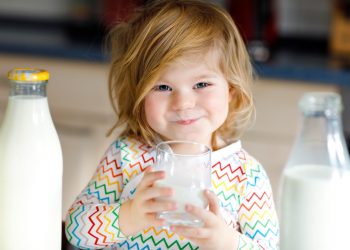 una bambina piccola che tiene in mano un bicchiere di latte, un alimento ricco di calcio