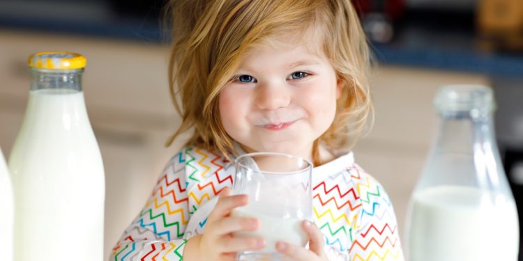 una bambina piccola che tiene in mano un bicchiere di latte, un alimento ricco di calcio
