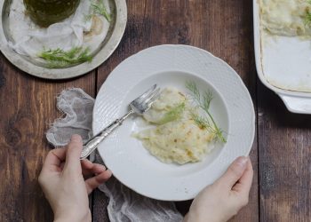 mani tengono una scodella bianca con finocchi gratinati, forchetta