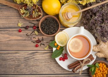 su tavolo di legno: in un piatto tazza piena di tisane con una fetta di limone , dietro spezie, pepe nero e miele