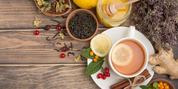 su tavolo di legno: in un piatto tazza piena di tisane con una fetta di limone , dietro spezie, pepe nero e miele