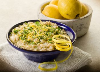 su sfondo chiaro ciotola blu con un risotto al limone e dietro ciotola con limoni biologici