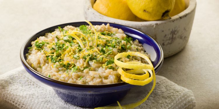 su sfondo chiaro ciotola blu con un risotto al limone e dietro ciotola con limoni biologici