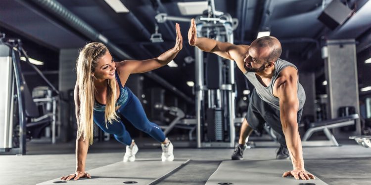 Uomo e donna in palestra che eseguono un plank e si danno il 5 perché sono riusciti ad eseguire l'esercizio di tonificazione