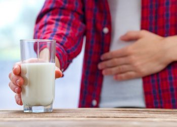 Un giovane si tiene una mano sulla pancia e nell'altra stringe un bicchiere di latte come sintomo dell'intolleranza al lattosio