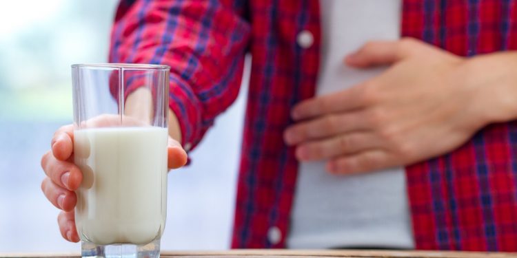 Un giovane si tiene una mano sulla pancia e nell'altra stringe un bicchiere di latte come sintomo dell'intolleranza al lattosio