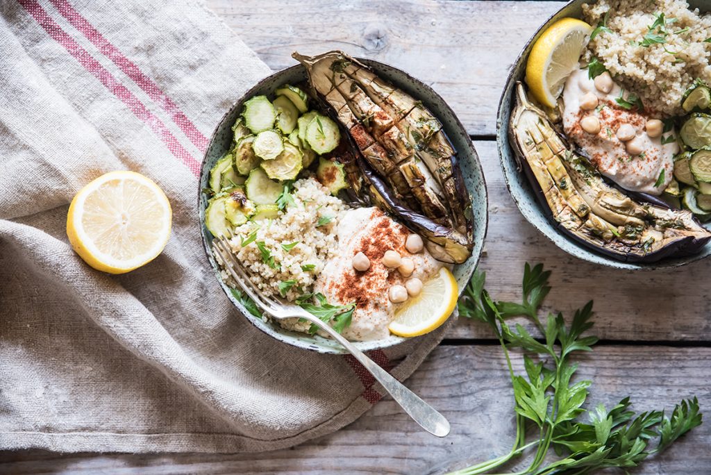 ricette vegetariane: su un tavolo di legno, un piatto di Buddha bowl con zucchine, melanzane e quinoa