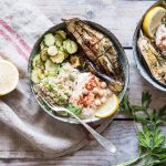 Su un tavolo di legno, un piatto di Buddha bowl con quinoa, zucchine e melanzane e accanto mezzo limone