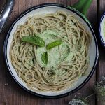 una scodella con spaghetti al pesto e foglie di basilico