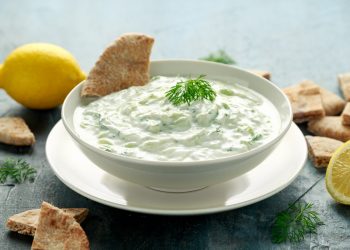 su un tavolo una ciotola con la salsa tzatziki , prezzemolo e fette di limone. Accanto crackers
