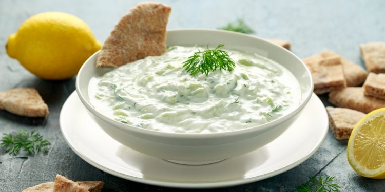 su un tavolo una ciotola con la salsa tzatziki , prezzemolo e fette di limone. Accanto crackers