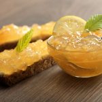 su base di legno una ciotola di vetro piena di marmellata di limoni e due fette di pane con marmellata di limoni spalmata sopra
