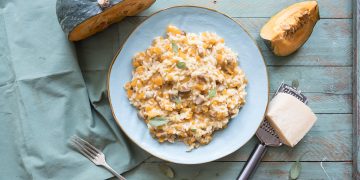 piatto azzurro su base azzurra pieno di risotto di zucca e porcini
