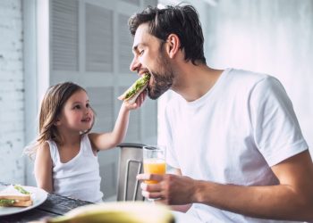 in una cucina, una bambina imbocca suo padre perché segue una dieta del panino. L'uomo tiene in mano una spremuta d'arancia. La bambina guarda il padre sorridendo e con tanto amore