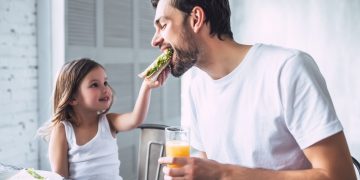 in una cucina, una bambina imbocca suo padre perché segue una dieta del panino. L'uomo tiene in mano una spremuta d'arancia. La bambina guarda il padre sorridendo e con tanto amore