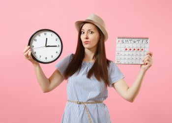 Una giovane donna che tiene in mano un orologio e un calendario per segnare le mestruazioni