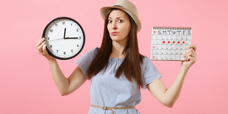 Una giovane donna che tiene in mano un orologio e un calendario per segnare le mestruazioni