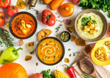 tante ciotole piene di minestre diverse e tante verdure sparse su base bianca