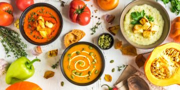 tante ciotole piene di minestre diverse e tante verdure sparse su base bianca